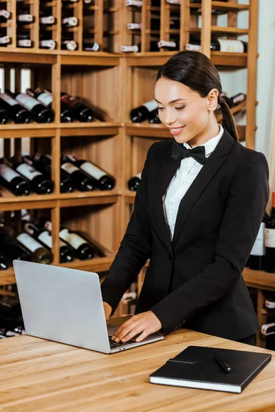 Bela mordomo do vinho do sexo feminino trabalhando com laptop na loja de vinhos — Fotografia de Stock