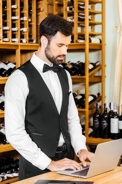 Beau jeune steward du vin travaillant avec ordinateur portable au magasin de vin — Photo de stock