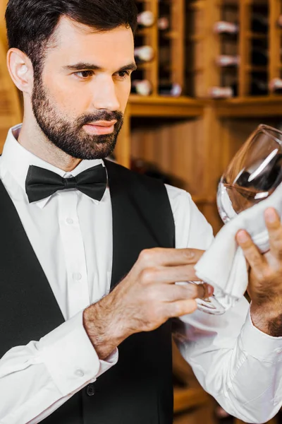 Apuesto joven camarero de vino limpiando vidrio en la tienda de vinos - foto de stock