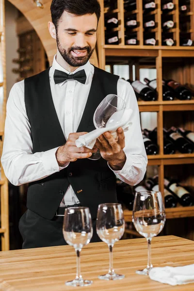 Jovem mordomo sorrindo verificando vidro limpo na loja de vinhos — Fotografia de Stock