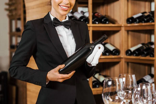 Tiro recortado de vinho feminino sorridente mordomo segurando garrafa na loja de vinho — Fotografia de Stock