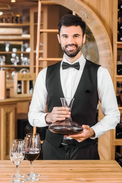 Bonito jovem sommelier segurando decantador de vinho tinto na loja de vinhos — Fotografia de Stock