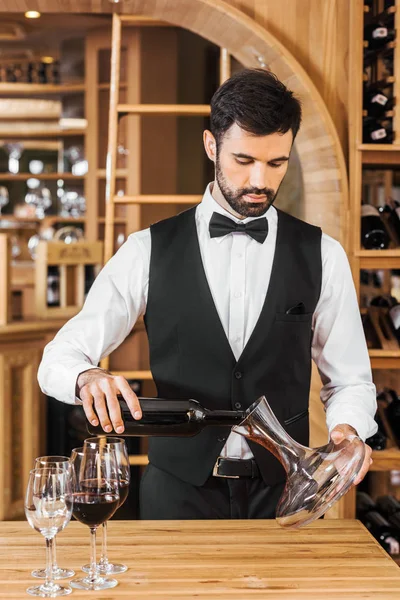 Apuesto joven administrador de vino verter vino en decantador en la tienda de vinos - foto de stock