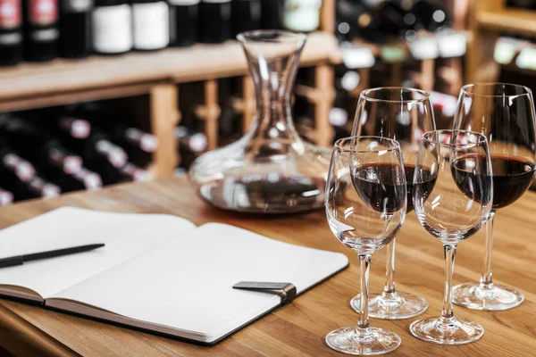 Close-up shot of decanter of red wine with notebook and glasses on wooden table at wine storage — Stock Photo