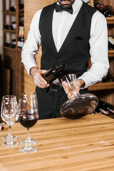 Tiro cortado de vinho mordomo derramando vinho de decantador na loja de vinho — Fotografia de Stock