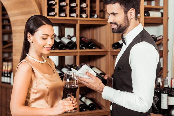 Vinho mordomo mostrando garrafa de vinho de luxo para a jovem na loja de vinhos — Fotografia de Stock