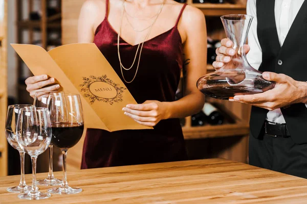 Tiro recortado de vinho mordomo segurando decanter enquanto o cliente ler lista de menu na loja de vinhos — Fotografia de Stock