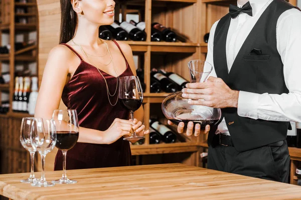 Tiro recortado de mayordomo de vino celebración decantador de vino en frente de cliente femenino en la tienda de vinos - foto de stock