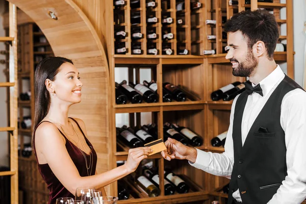 Steward de vin prenant la carte de crédit du client féminin au magasin de vin — Photo de stock