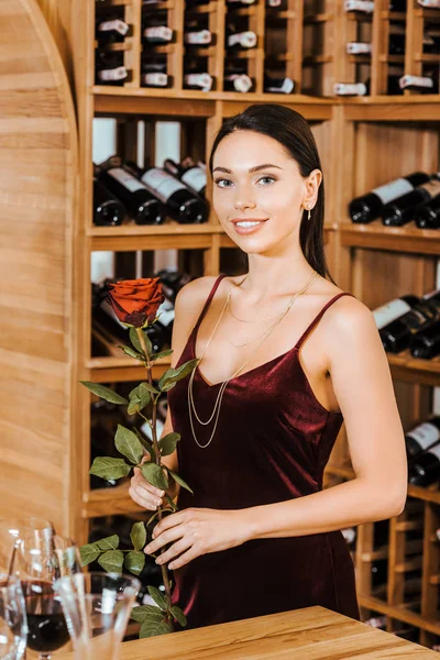 Belle femme en robe rouge avec fleur rose au magasin de vin — Photo de stock