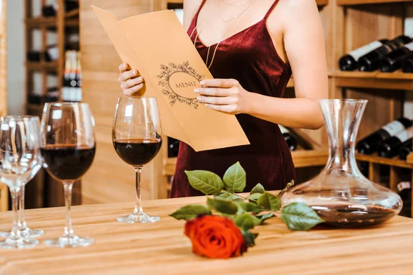 Tiro recortado de la mujer en vestido rojo tarjeta de menú de lectura en la tienda de vinos - foto de stock