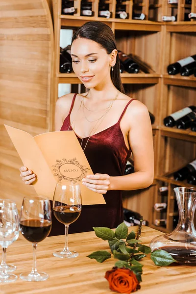 Hermosa mujer en vestido rojo lectura carta de vino en la tienda de vinos - foto de stock