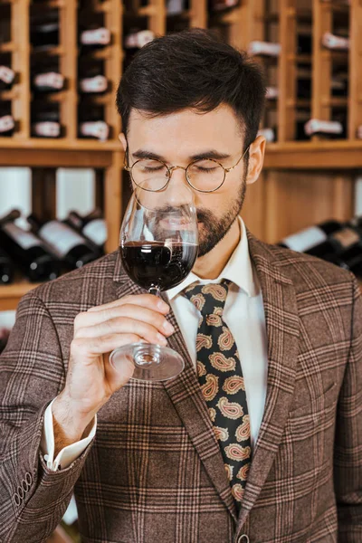 Apuesto joven sommelier examinar aroma de vino de vidrio en tienda de vinos - foto de stock