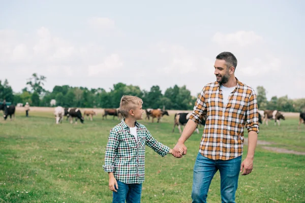 Glücklicher Vater und Sohn Händchen haltend und einander lächelnd auf dem Bauernhof — Stockfoto