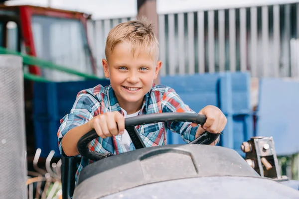 Niño feliz montando vehículo agrícola y sonriendo a la cámara - foto de stock