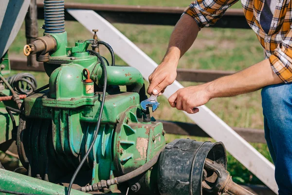 Cropped shot of farmer holding wrench and fixing engine — Stock Photo