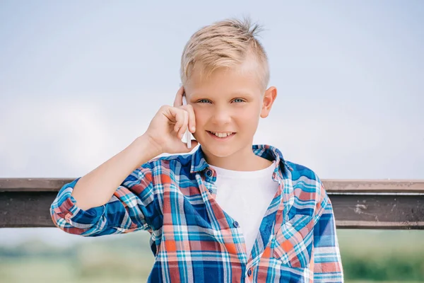 Glückliches Kind, das per Smartphone spricht und in die Kamera lächelt — Stockfoto
