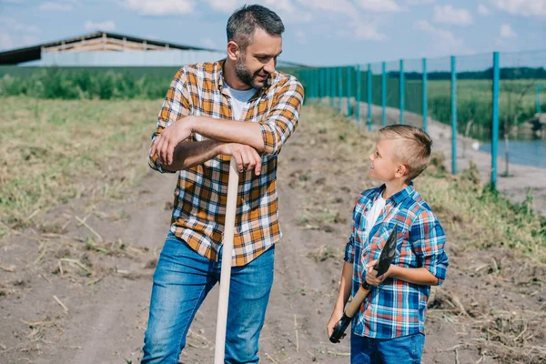 Батько і син тримають лопатки і дивляться один на одного на фермі — стокове фото