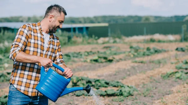 Farmer in checkered shirt holding watering can and working in field — Stock Photo