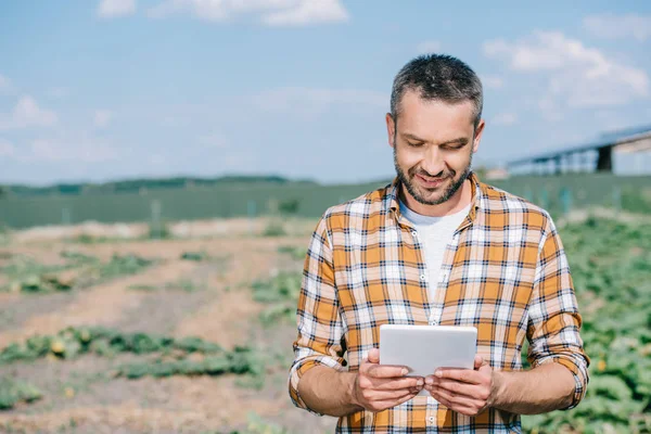 Красивый улыбающийся фермер, использующий цифровой планшет, стоя на поле — стоковое фото