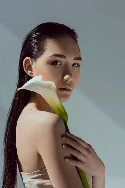 Atractiva mujer asiática con flor de calla, aislado en gris - foto de stock
