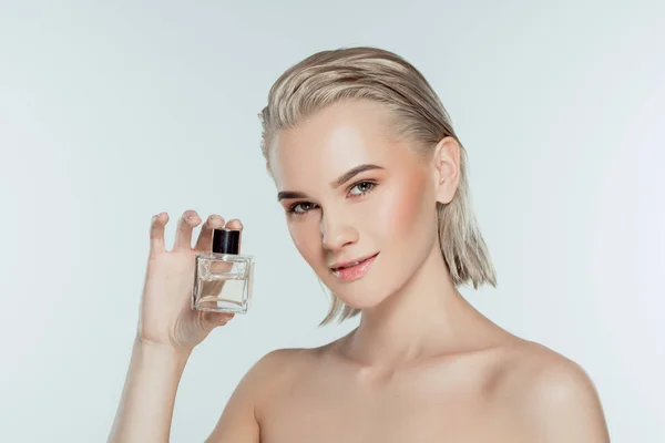Chica rubia desnuda sosteniendo botella de perfume, aislado en gris - foto de stock