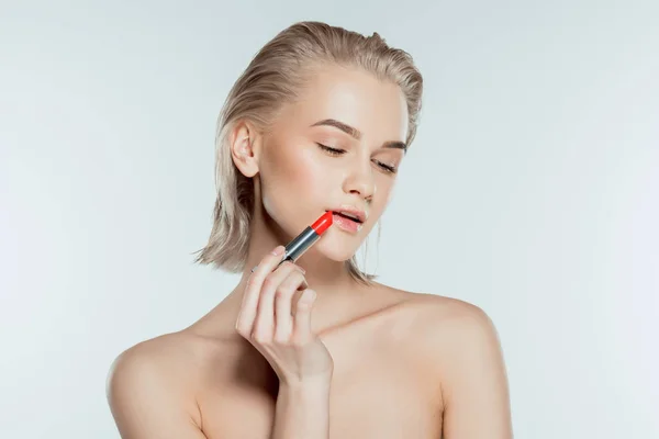 Attraktives zartes Mädchen, das roten Lippenstift aufträgt, isoliert auf grau — Stockfoto