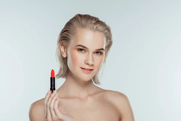 Beautiful blonde girl holding red lipstick, isolated on grey — Stock Photo