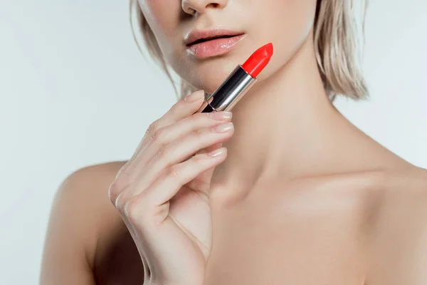 Cropped view of young woman holding red lipstick, isolated on grey — Stock Photo