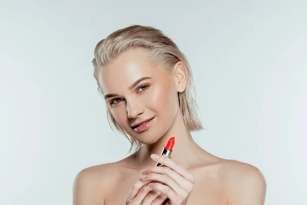 Happy beautiful woman holding red lipstick, isolated on grey — Stock Photo