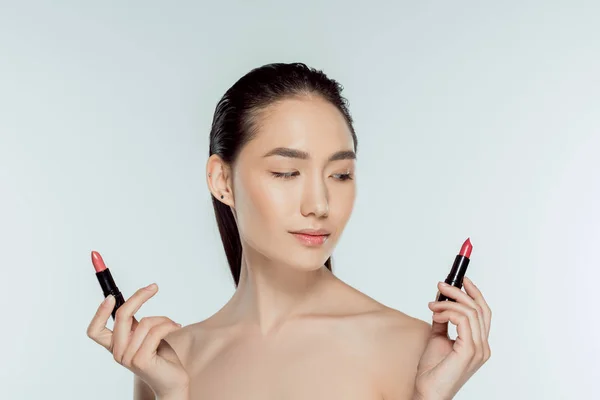 Bela asiática mulher escolher vermelho batons, isolado no cinza — Fotografia de Stock