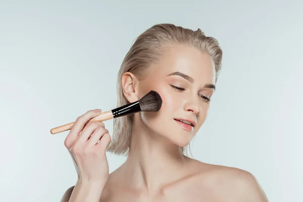 Hermosa mujer aplicando polvo con cepillo cosmético, aislado en gris - foto de stock