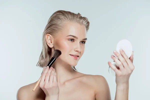 Blonde woman applying compact powder with cosmetic brush, isolated on grey — Stock Photo