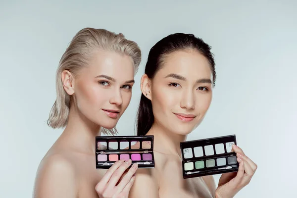 Multiethnic naked women posing with palettes of eyeshadows, isolated on grey — Stock Photo