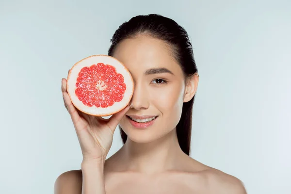 Приваблива азіатська дівчина позує з грейпфрутом, ізольована на сірому — стокове фото