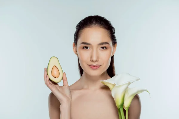 Beautiful asian girl posing with avocado and calla flowers, isolated on grey — Stock Photo