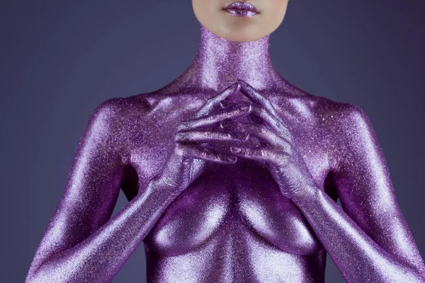 Обрезанный вид на модную девушку, окрашенную ультрафиолетовым блеском, выделенный на фиолетовый — стоковое фото