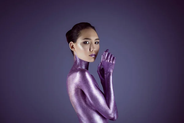 Привлекательная обнаженная модная азиатка в ультрафиолетовом блеске, изолированная на фиолетовом — стоковое фото