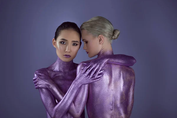 Chicas desnudas multiétnicas en brillo ultravioleta abrazándose juntas, aisladas en púrpura - foto de stock
