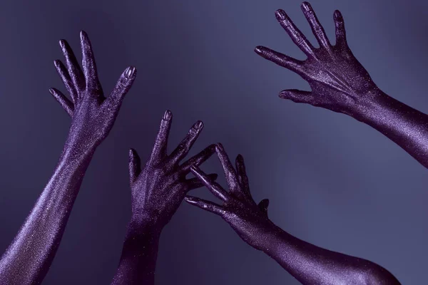 Vista parcial de las manos femeninas en brillo ultravioleta, aislado en púrpura - foto de stock