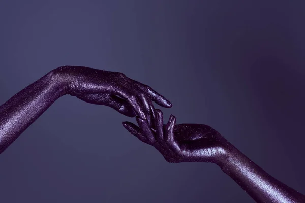 Vista parcial de las manos de las mujeres en brillo ultravioleta tocándose entre sí, aislado en púrpura - foto de stock