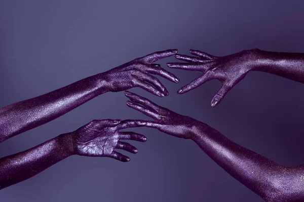 Cropped view of girls hands in glitter touching each other, isolated on purple — Stock Photo