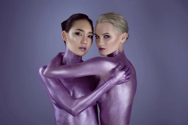 Багатоетнічні оголені дівчата в ультрафіолетовому блиску, що обіймаються для модної стрільби, ізольовані на фіолетовому — стокове фото