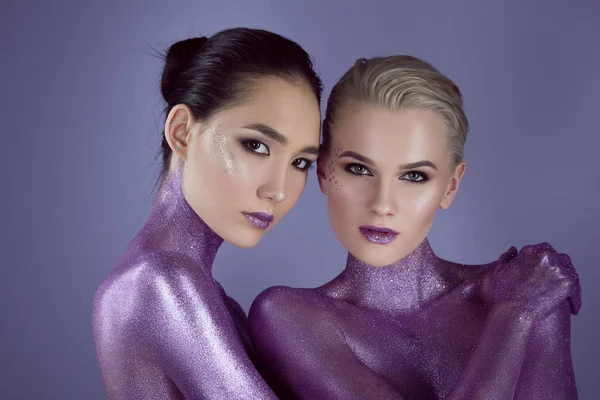 Многоэтнические красивые девушки в ультрафиолетовом блеске, обнимающие вместе, изолированные на фиолетовый — стоковое фото