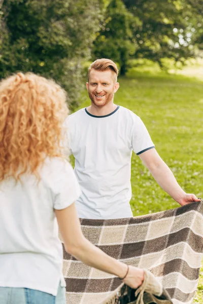 Feliz casal ruiva olhando uns para os outros e segurando xadrez no piquenique no parque — Fotografia de Stock