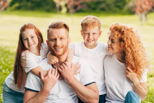 Beautiful happy redhead family hugging and smiling at camera in park — Stock Photo