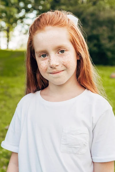 Retrato de adorável criança de cabelos vermelhos sorrindo para a câmera no parque — Fotografia de Stock