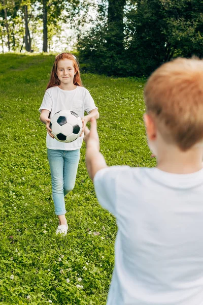 Plan recadré de frère et soeur jouant avec le ballon de football au parc — Photo de stock