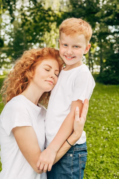 Feliz joven madre abrazando adorable pequeño hijo en parque - foto de stock