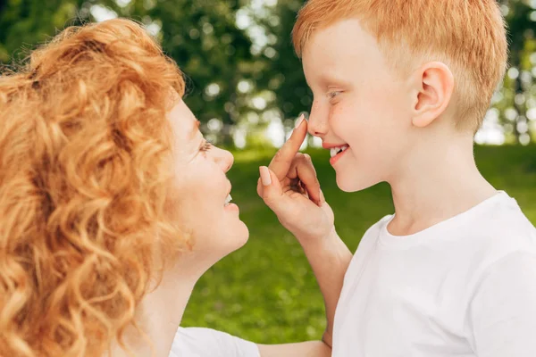 Vista lateral da mãe ruiva feliz e filho sorrindo uns aos outros no parque — Fotografia de Stock